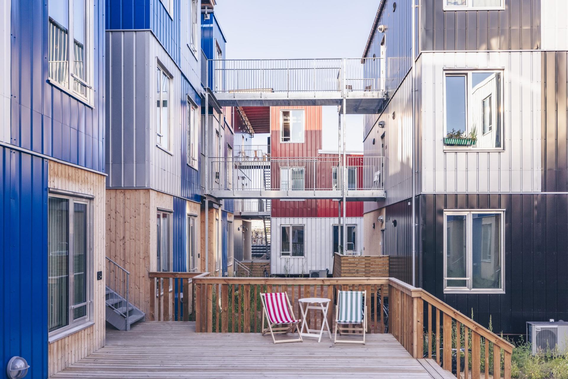 Sustainable micro-homes in CPH Village with colorful facades, wooden terraces, and seating areas in the courtyard environment.